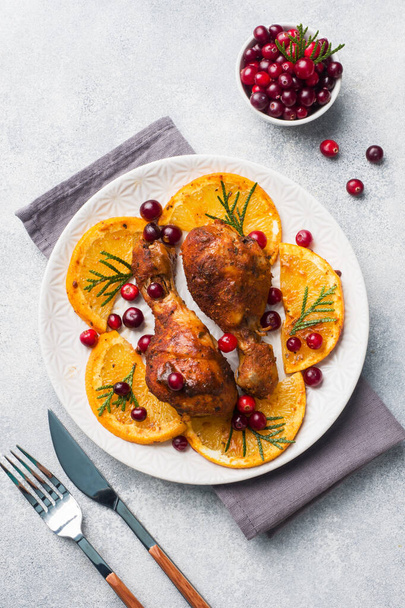 Baked chicken drumstick with oranges and cranberries in a plate light grey background. Christmas food Table with decorations. Copy space. - Фото, зображення