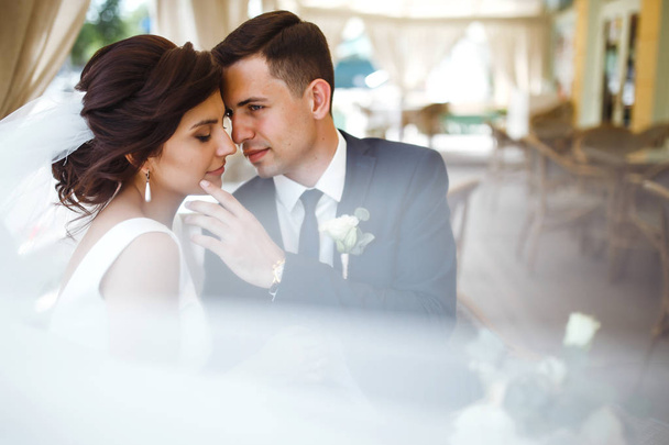 Young bride and groom in a cafe. Husband and wife hold each other's hands. Loving couple in a restaurant. Groom kissing a bride. Pretty bride and stylish groom. Wedding day. Marriage. - Photo, Image