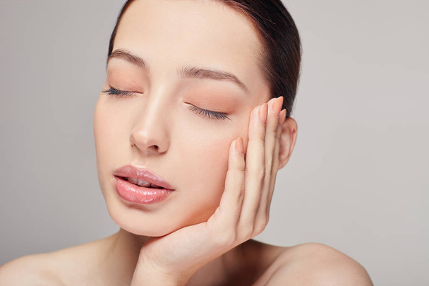 An elegant sophisticated beautiful girl, brown hair and clean delicate skin on the gray background. Lady put her head on her hand. Close eyes. Spa, face skin care. Wellness. - Photo, image