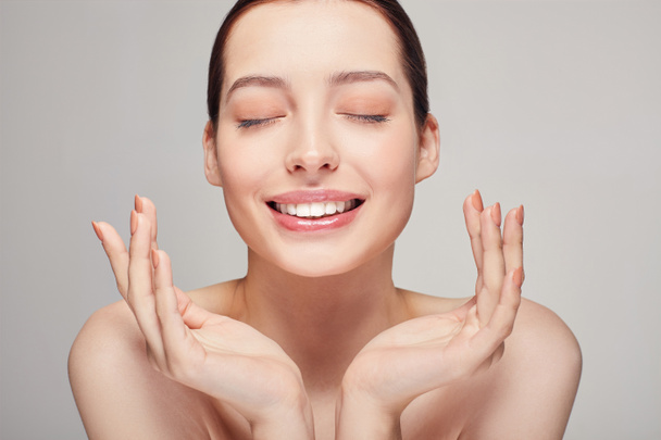 An elegant sophisticated beautiful girl with full lips, dark hair and radiant clean delicate skin on background. Happy lady holding her both hands near her face. Skin care, spa, beauty. - Photo, Image