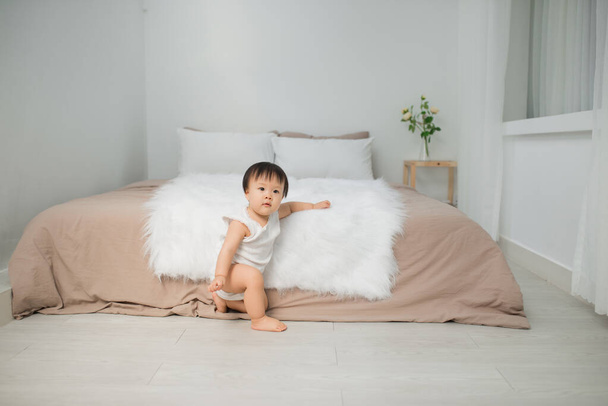 Mała dziewczynka siedzi w pobliżu łóżka w domu. Kid w: Home Concept. - Zdjęcie, obraz