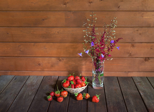 Fresh ripe strawberry and bouquet made of red astilbe and blue bell flowers on wooden table. - Photo, Image