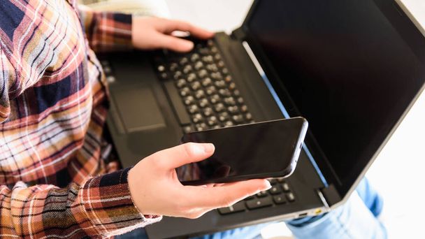 girl holds smartphone and laptop in hands, selective focus on the hand - Photo, Image