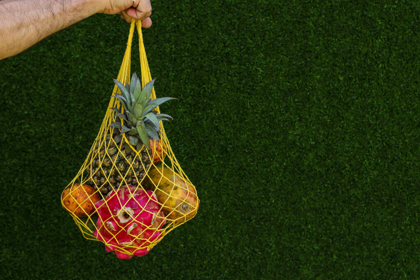 Тропічні фрукти: манго, папайя, ананас, дракон і фрукти пристрасті в жовтій сумці з текстилю на зеленому тлі, горизонтальна орієнтація
 - Фото, зображення