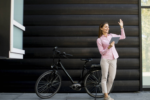 Happy young woman with files in the hands standing outdoor next to electric bike - 写真・画像