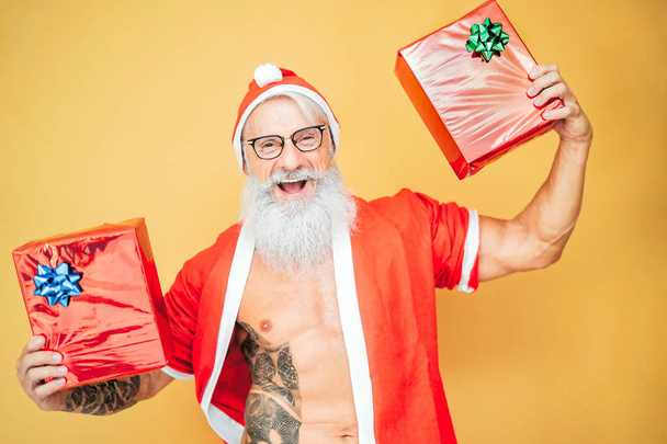 Ευτυχισμένος Άγιος Βασίλης κρατώντας χριστουγεννιάτικα δώρα - Trendy γενειοφόρος hipster ανώτερος διασκεδάζοντας φορώντας ρούχα Χριστούγεννα - Ηλικιωμένοι άνθρωποι γιορτάζουν τις διακοπές πολιτισμού τρόπου ζωής - Φωτογραφία, εικόνα