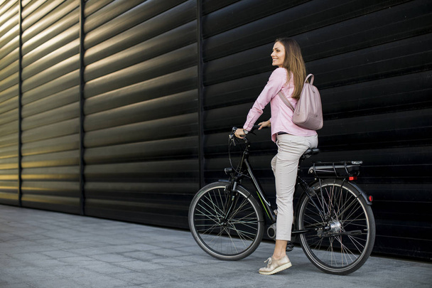 Pretty young woman riding an electric bicycle in urban environment - 写真・画像