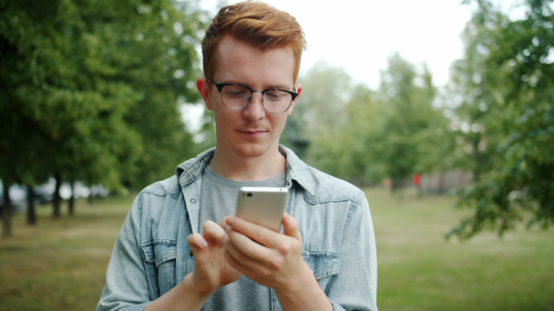 Fiatal férfi használ okostelefon a parkban érintőképernyő élvezi a modern eszköz - Felvétel, videó