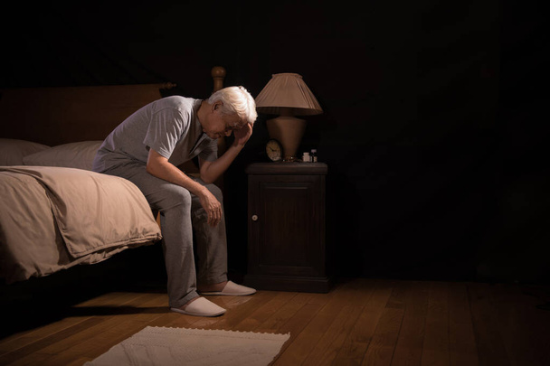 Депрессивный пожилой человек, сидящий в постели, не может спать от бессонницы
 - Фото, изображение