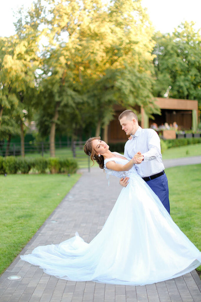 junge Braut tanzt mit Bräutigam im Park und trägt weißes Kleid. - Foto, Bild