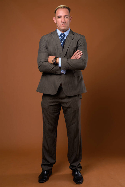 Full body shot of businessman standing against brown background - Foto, Imagen