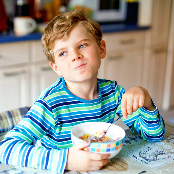 Adorable little blond school kid boy eating cereals with milk and berries for breakfast or lunch. Healthy eating for children, schoolkids. At school canteen or at home - Photo, Image