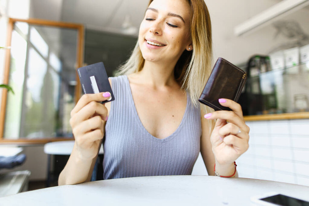 Blonde girl sitting at cafe and keeping wallet with debit card. - 写真・画像
