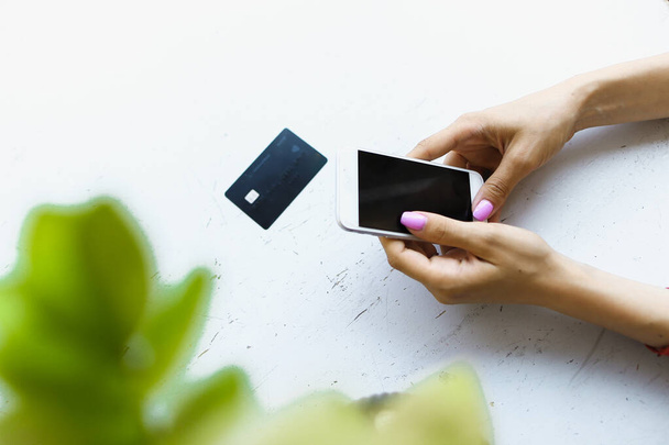 Female caucasian hands keeping credit card and smartphone in white background. - Foto, Bild