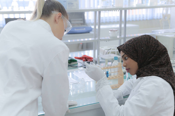 Two multiethnic young female scientists doing experiments in lab - Фото, изображение