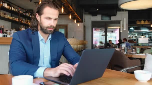 Distant view of a young businessman sitting at a table in a cafe using the phone. Successful people, daily routine. Entertaining, relaxing, chatting. - Footage, Video