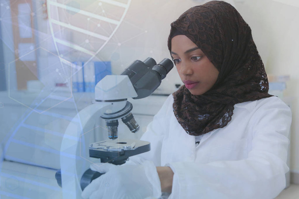 Genç Afrikalı Müslüman kadın bilim adamı mikroskoba bakıyor. - Fotoğraf, Görsel