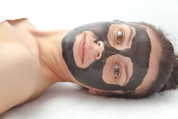 Νεαρή όμορφη γυναίκα με μαύρη μάσκα προσώπου από κάρβουνο. Δέρμα  - Φωτογραφία, εικόνα