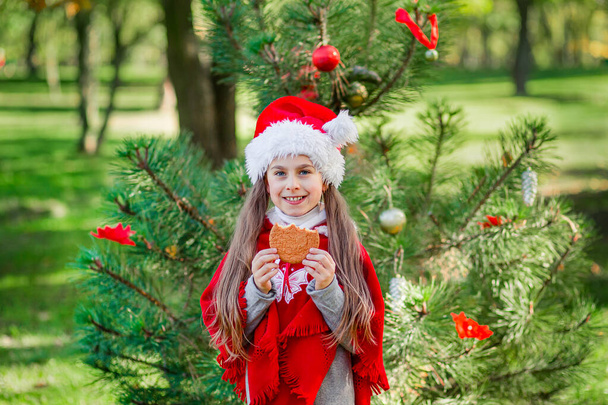 Roztomilé děvče jíst vánoční cukroví na pozadí novoroční stromeček. Zimní dovolená a lidé koncept. - Fotografie, Obrázek