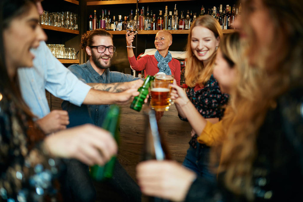 Φίλοι που στέκονται στο μπαρ και κάνουν πρόποση με μπύρα. - Φωτογραφία, εικόνα