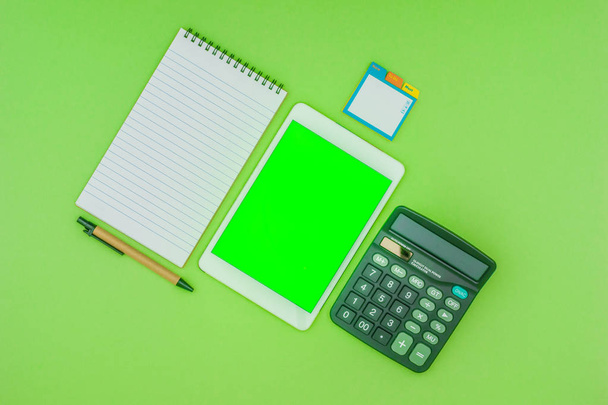 Business office and school stationery, green screen tablet, on green background. Flat lay top down concept. - Photo, Image