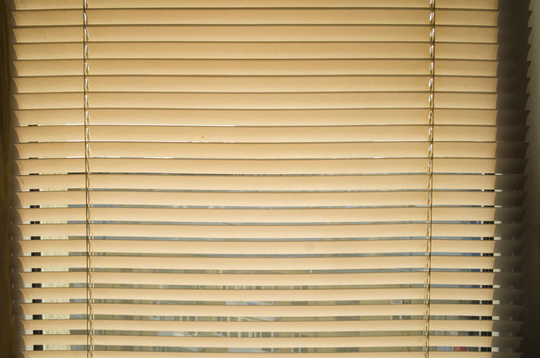 A nap átsüt a műanyag redőnyön az ablakon. Zárt jalousie szoba belső tér. - Fotó, kép