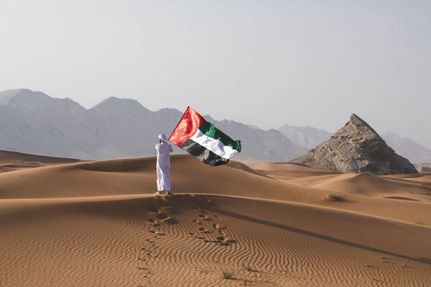 Homem árabe segurando a bandeira dos EAU no deserto celebrando o dia nacional dos EAU e o dia da bandeira dos EAU
. - Foto, Imagem