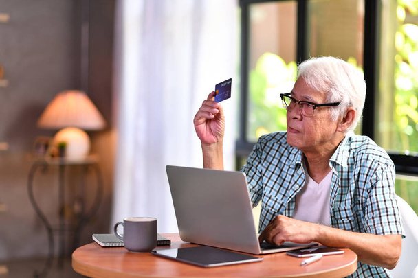 Hombre mayor asiático buscando confundir cuando se utiliza la tarjeta de crédito para las compras en línea
 - Foto, Imagen