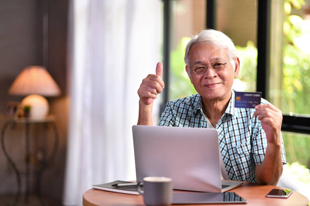 Aasian vanhempi mies käyttää luottokorttia verkkokaupoissa
 - Valokuva, kuva