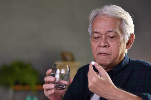 Asian senior man taking pills at home - Foto, afbeelding