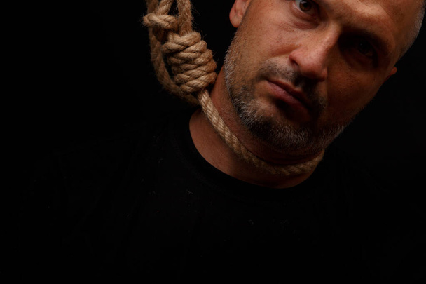 Suicidal man with a noose around his neck on a dark background - 写真・画像