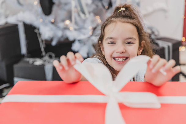 Closeup photo of super excited young girl opening large christmas present while sitting on living room floor. - Foto, afbeelding