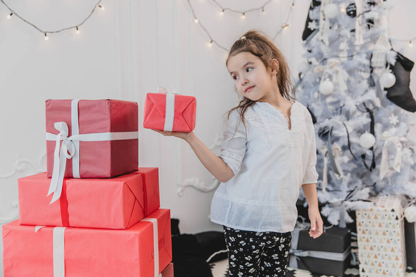 Lovely little girl playing with Christmas giftboxes, building a pyramid. - Foto, imagen