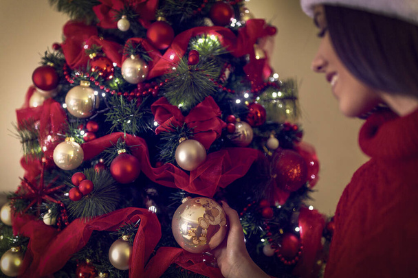 Woman in Santa hats placing a ornament on a Christmas tree.  - Foto, Bild