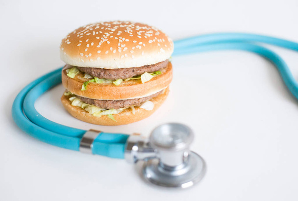 Гамбургер і медичний стетоскоп на білому тлі, копіювання простору. Ефекти здоров'я нездорової їжі
 - Фото, зображення