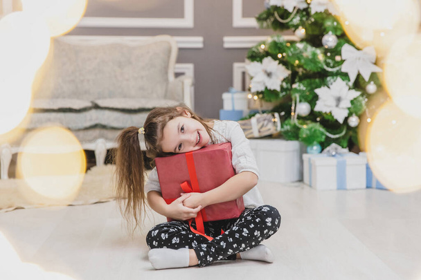 Light photo of cute kid sitting with gift in hands, like a little gnome in christmas decorated room. - Foto, afbeelding