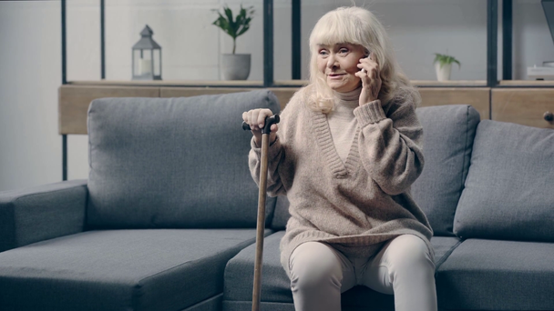 Senior woman talking on smartphone on sofa - Záběry, video