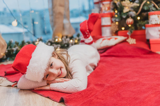 Santa claus kid laying on the red blanket under Christmas tree. - Фото, изображение