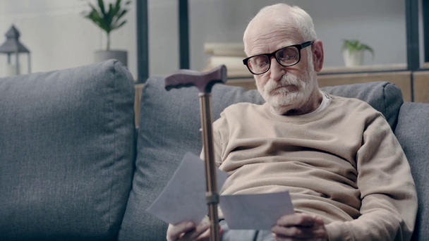 Starszy mężczyzna z demencją oglądający zdjęcia na sofie - Materiał filmowy, wideo