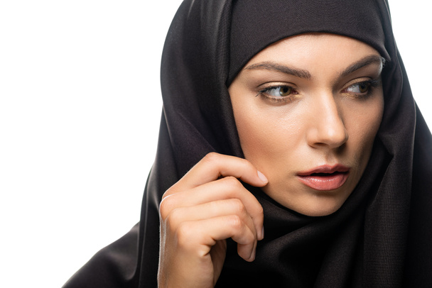 krásná mladá muslimka dotýkající se hidžábu a odvracející se izolované na bílém - Fotografie, Obrázek
