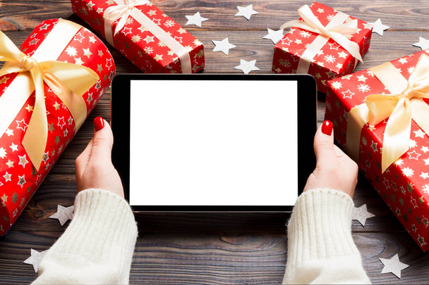 Top kilátás női kéz kezében egy tabletta fa karácsonyi háttér készült ajándékdobozok és hópelyhek. Újévi ünnepi koncepció. Mockup - Fotó, kép