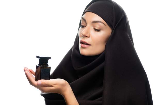 jonge moslim vrouw in hijab houden fles parfum geïsoleerd op wit - Foto, afbeelding