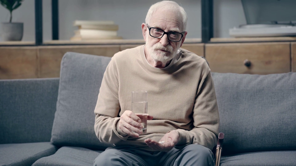 Senior man with dementia holding pills and glass of water  - Footage, Video