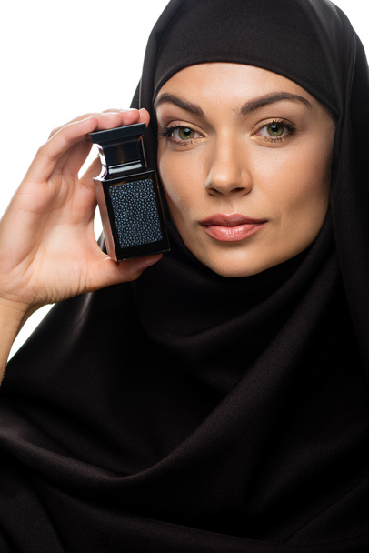 young Muslim woman in hijab holding bottle of perfume isolated on white - Фото, изображение