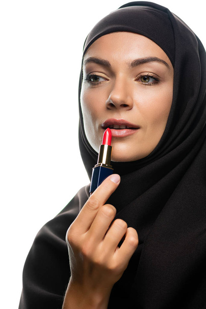 joven musulmana en hiyab aplicando lápiz labial rojo aislado en blanco
 - Foto, Imagen