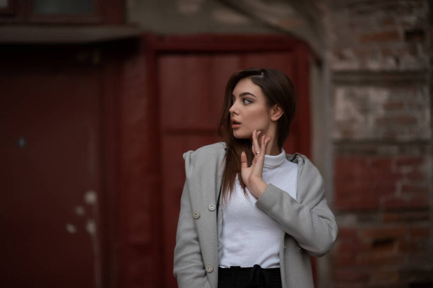 fiatal lány áll a háttérben egy városi utcában. Szürke kabátos lány. Egy fotósorozat egy barnával - Fotó, kép