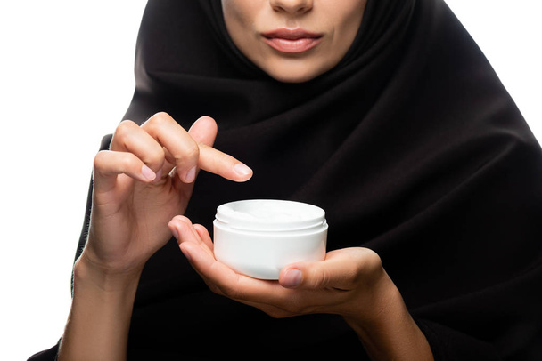 bijgesneden weergave van jonge moslimvrouw in hijab aanbrengen crème geïsoleerd op wit - Foto, afbeelding