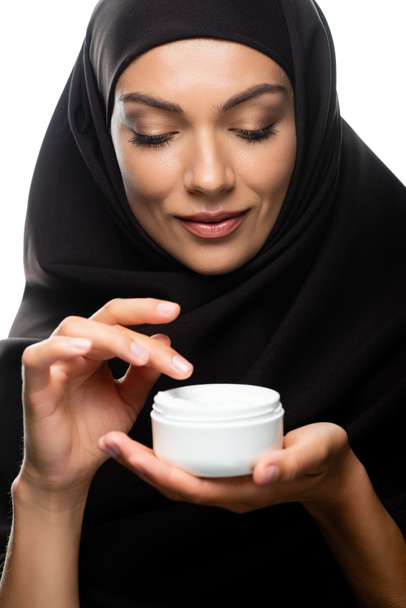 young Muslim woman in hijab holding container with cosmetic cream isolated on white - Photo, Image