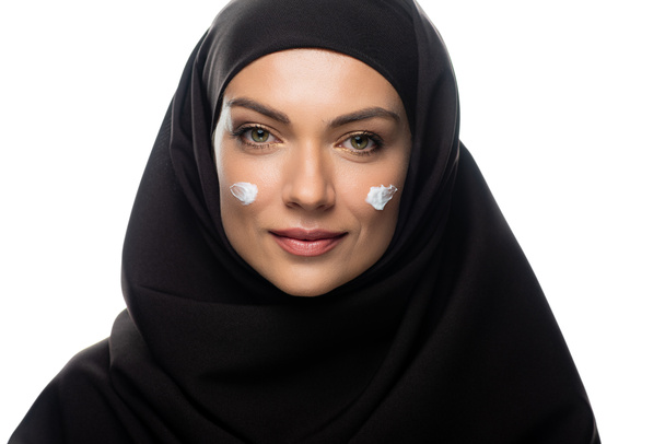 νεαρή μουσουλμάνα γυναίκα με μαντίλα με καλλυντική κρέμα σε νεοσσούς απομονωμένους σε λευκό - Φωτογραφία, εικόνα