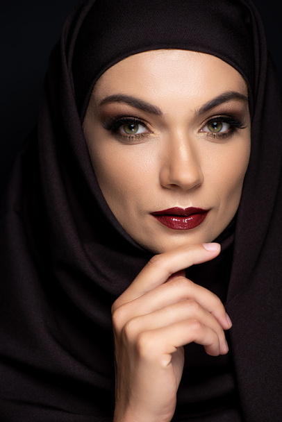 mladá muslimka v hidžábu s kouřícíma očima a rudými rty izolované na černé - Fotografie, Obrázek